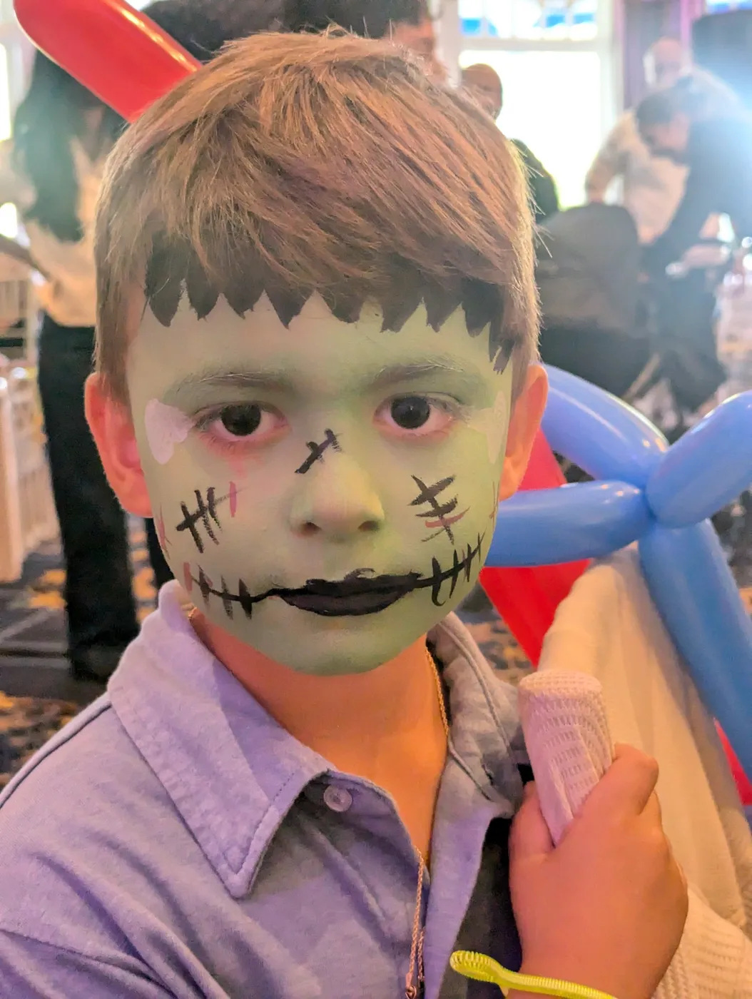 A child wearing a green monster face-painting design